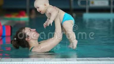 一个女人在一个室内<strong>游泳池</strong>里扔出一个一岁的饱<strong>婴儿</strong>。 孩子开心地笑了.. 妈妈`健康的一天